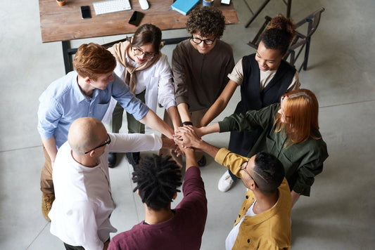 A team gathered together with their hands in the circle to symbolize teamwork in the workplace environment.