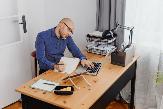 A man working on the computer and writing while on the phone multitasking