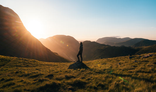 A man standing on a rock in a hilly area looking at the sunrise to signify self-development and personal growth